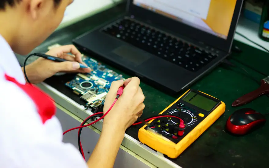 Technician testing and recertifying a refurbished laptop on a bench.